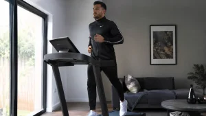 Homme en survêtement courant sur un tapis de course pour favoriser la perte de graisse abdominale.
