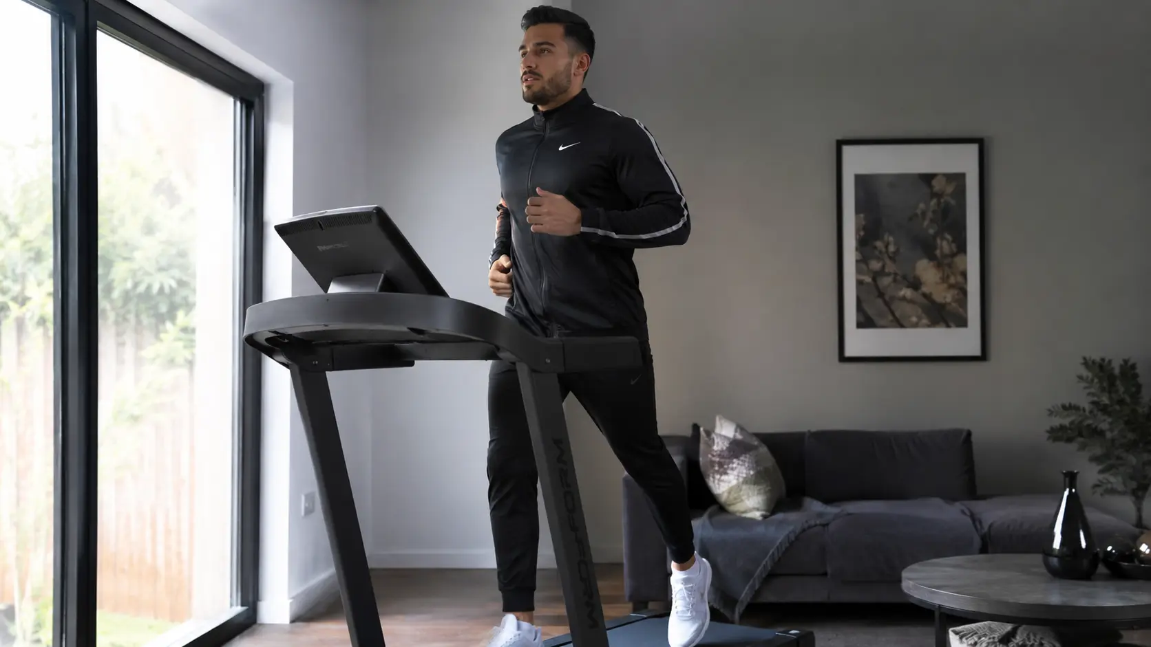 Homme en survêtement courant sur un tapis de course pour favoriser la perte de graisse abdominale.