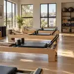 Salle de Pilates lumineuse avec reformers en bois, tapis et accessoires rangés